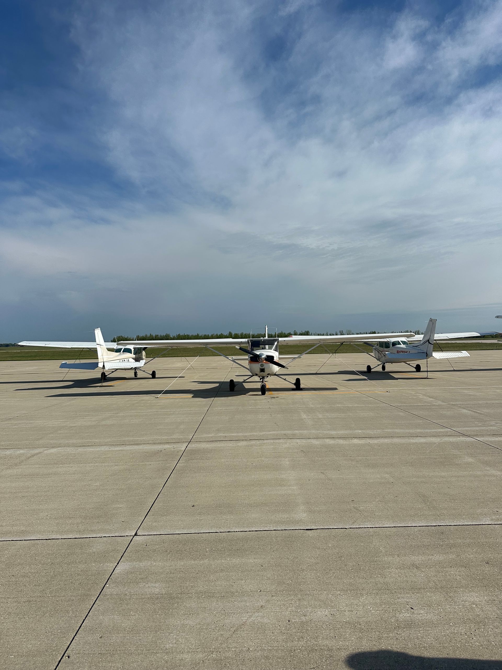 Three small airplanes parked on a concrete runway under a cloudy sky.