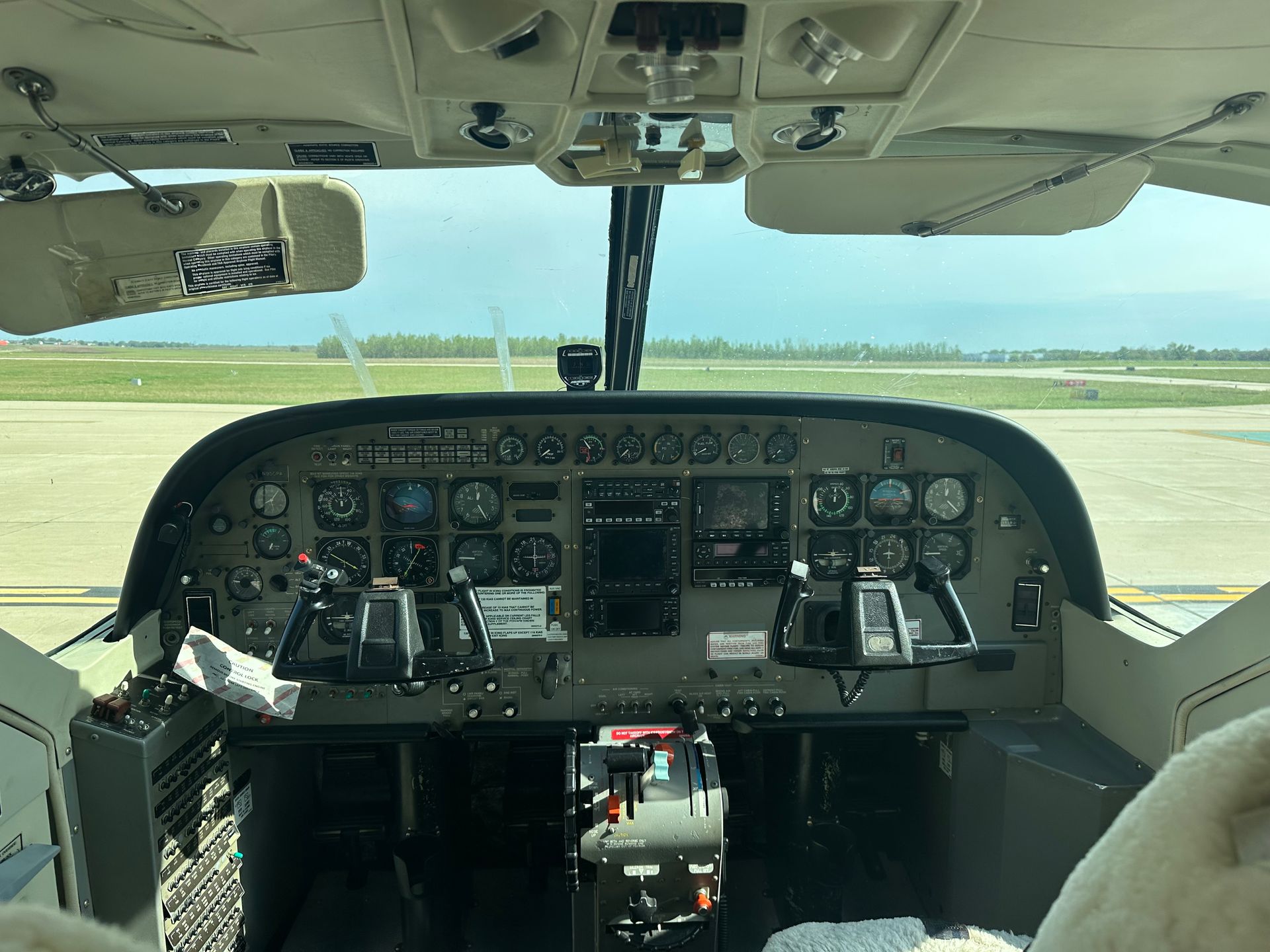 Cockpit view from a small plane on the runway, with green fields visible ahead