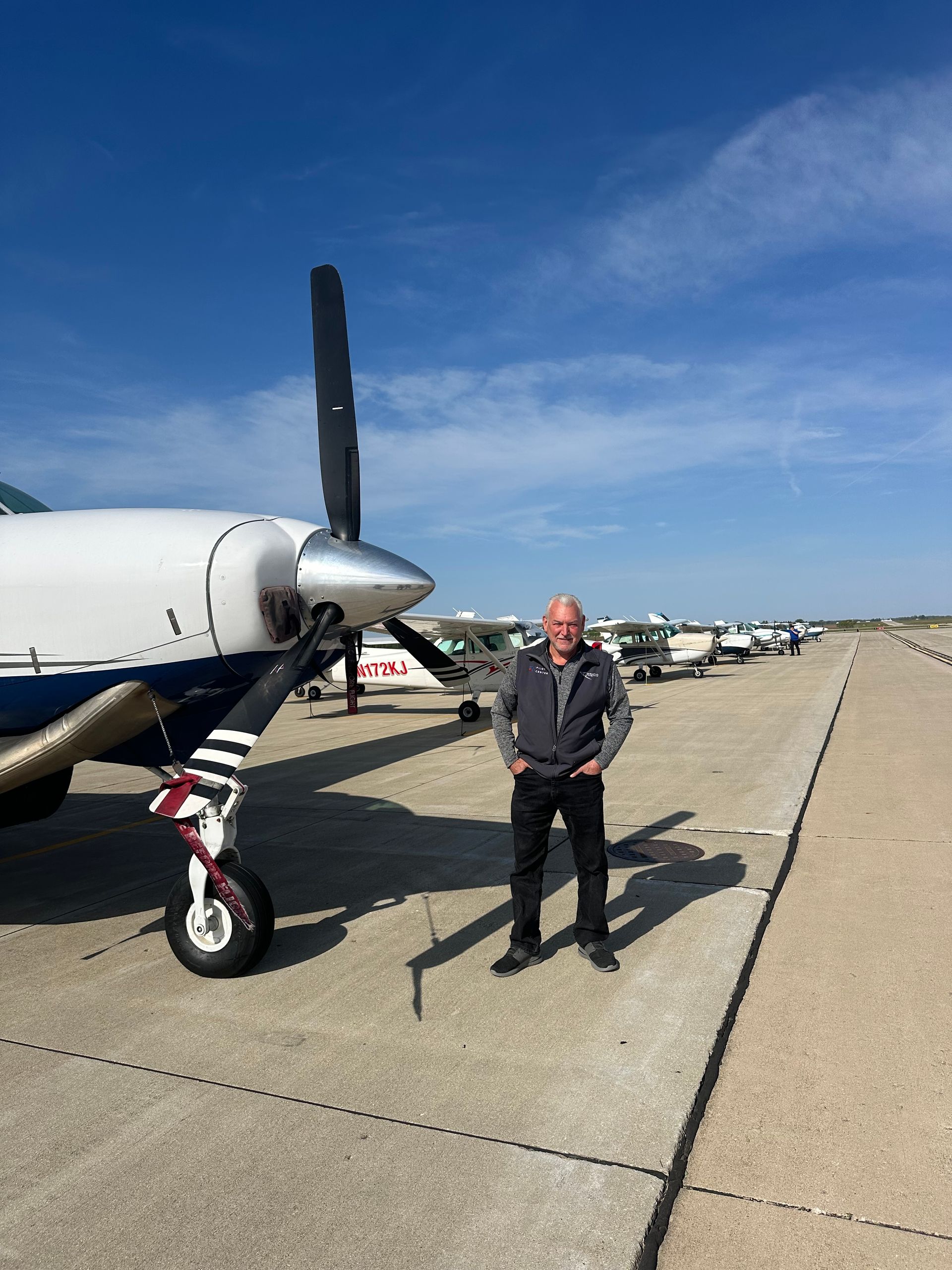 Man standing beside a small airplane on a sunny airport tarmac under a clear blue sky.