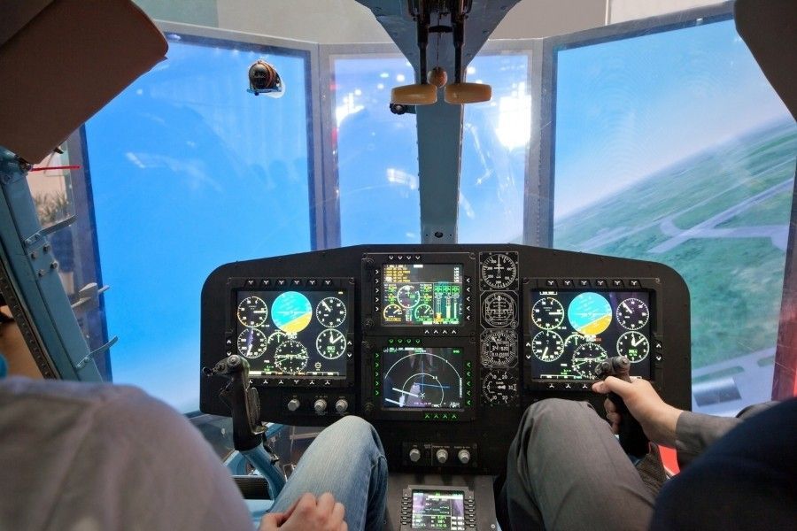 Students operating helicopter flight simulator with digital instrument panel and panoramic display.
