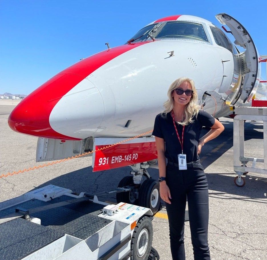 Student pilot Lauren Cain standing beside Embraer 145 jet during pilot training or airline operations.