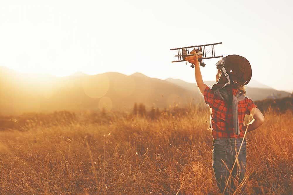 A little boy holding up a toy airplane in a grassy field.