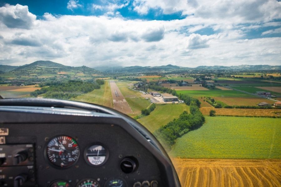 Pilot cockpit view approaching runway over farmland during flight training.