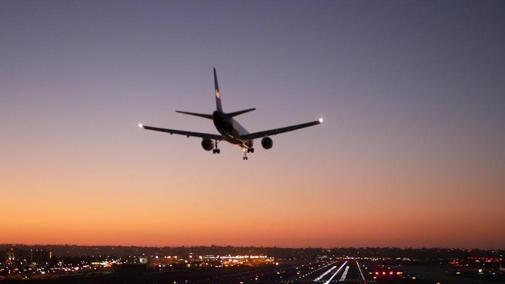 Airplane landing at sunset over a runway with city lights below.