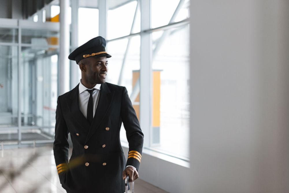 An airline pilot walks through the terminal in uniform with a suitcase.