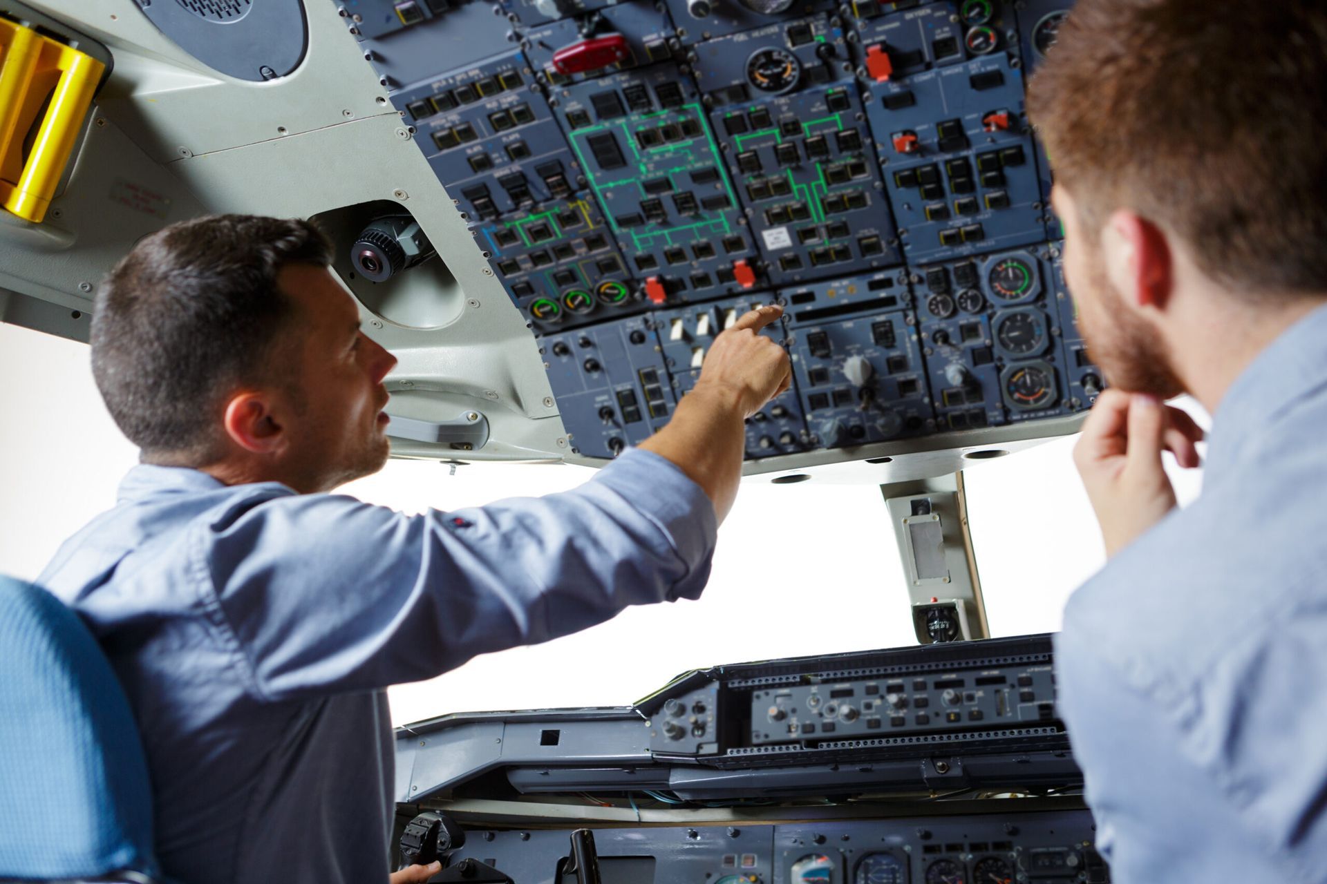 Instructor demonstrating overhead cockpit controls to student in an airline training simulator.