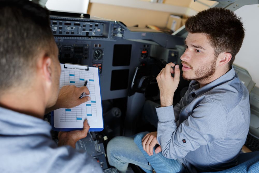 Two men are sitting in a cockpit of an airplane looking at a clipboard.