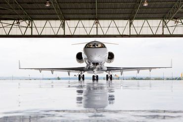 Business jet parked in a hangar with its nose facing out toward the runway.