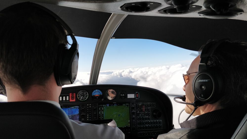 Flight instructor and student flying above clouds in a modern glass-cockpit training aircraft.
