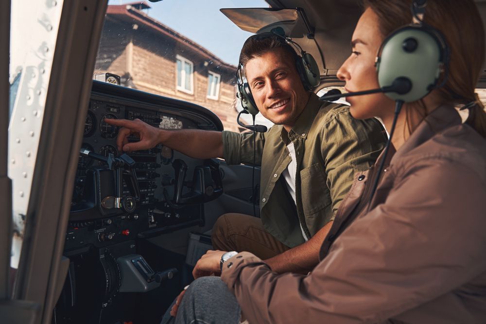 Flight instructor guiding student through cockpit controls during pilot training session.