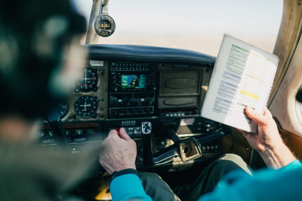 Instructor and student in a light aircraft cockpit reviewing a printed checklist while practicing flight procedures.