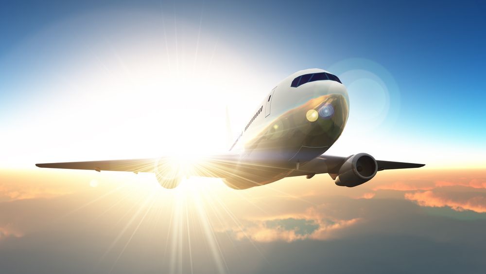 A plane flying in the sky with the sun shining behind it.