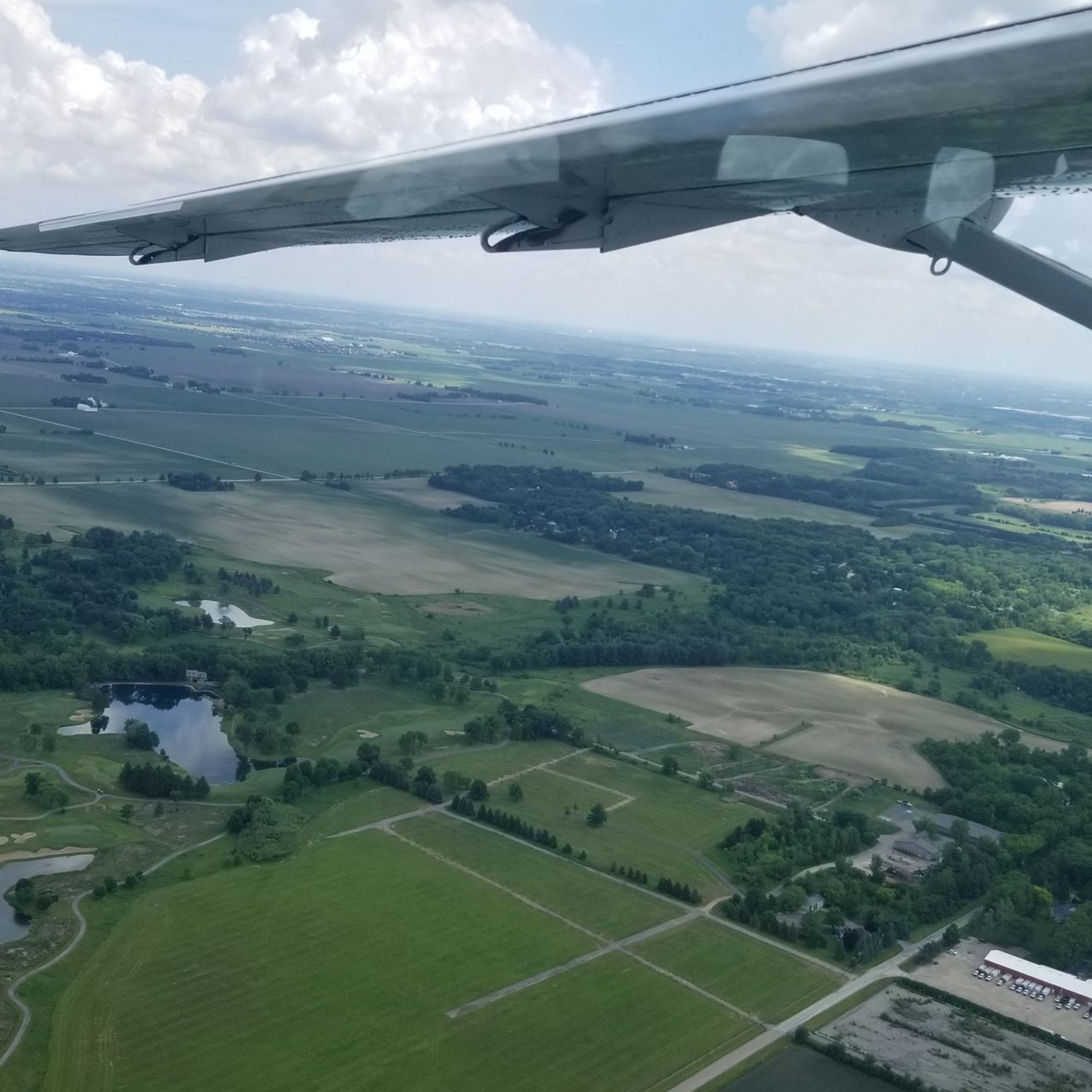 Aerial view from a small plane over green fields, roads, and a patchwork rural landscape