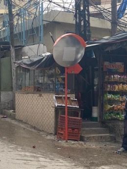 A man is standing in front of a store with a mirror on the side of the road.