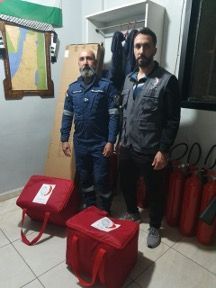 Two men standing in a room with red bags and fire extinguishers