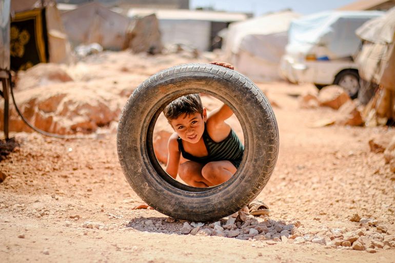 A young boy is playing in a tire in the dirt.