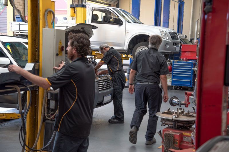 Mechanics working in a vehicle repair shop with a white pickup on a lift