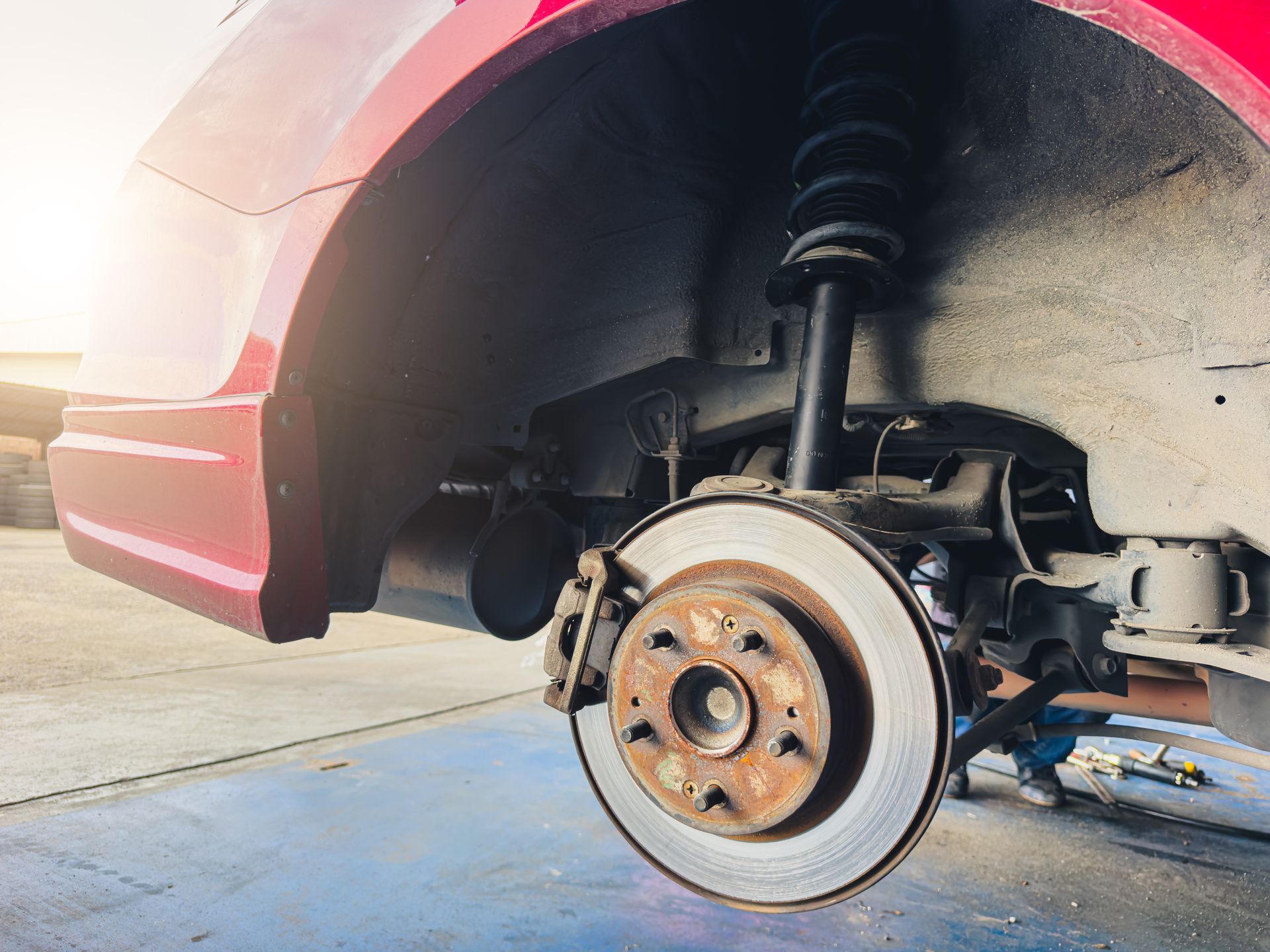 Car’s front wheel removed, exposing rusty brake rotor and suspension in a garage.