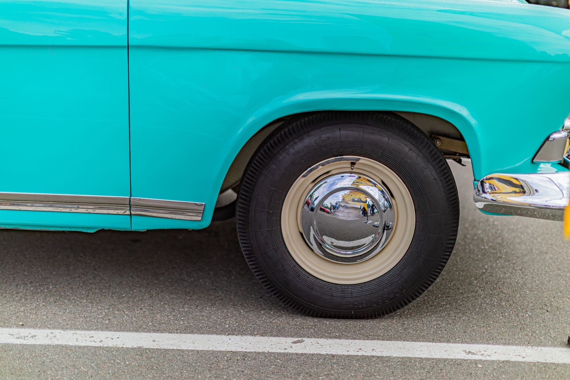 Turquoise vintage car side panel and front wheel parked on pavement