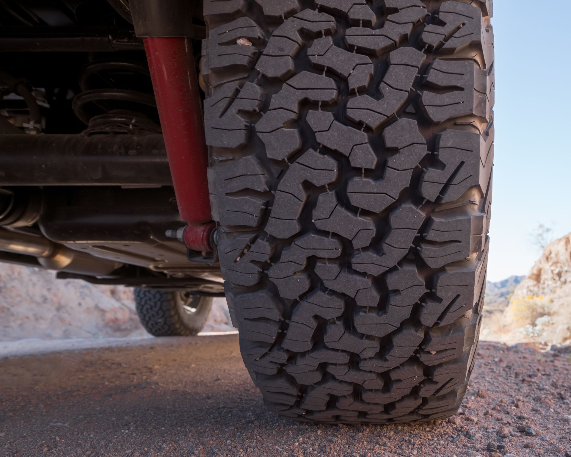 Close-up of an off-road tire with deep tread on a vehicle parked on gravel and dirt.
