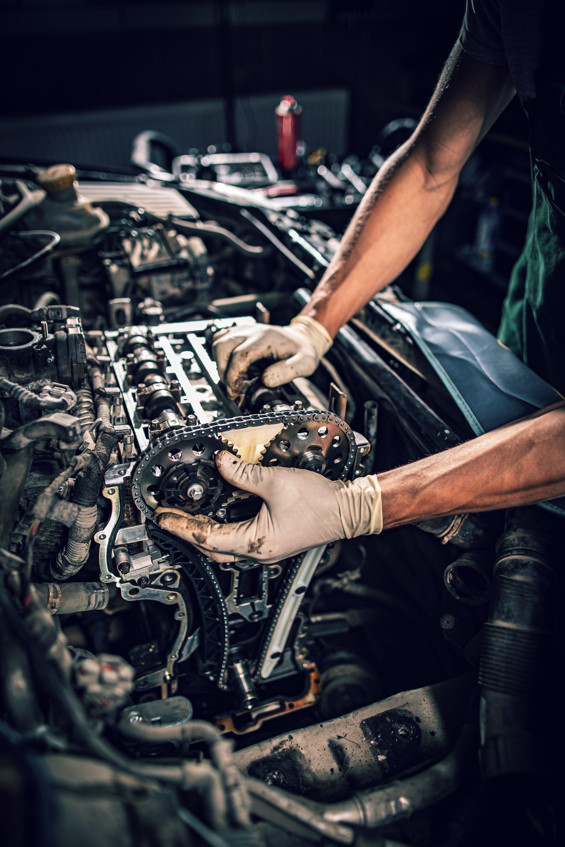 Mechanic's gloved hands working on an exposed car engine in a dim garage