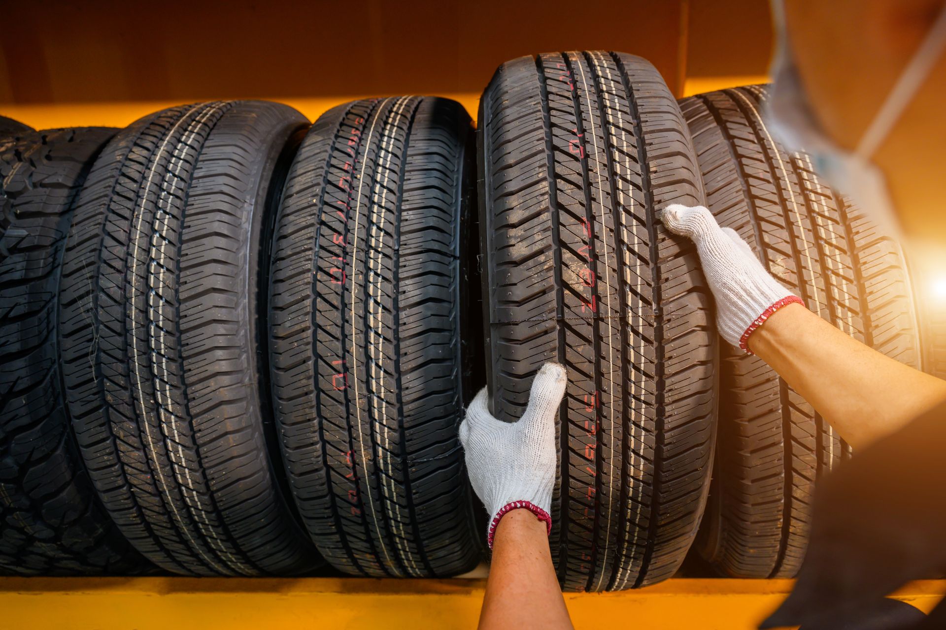 Gloved hands inspecting a row of black car tires on an orange rack