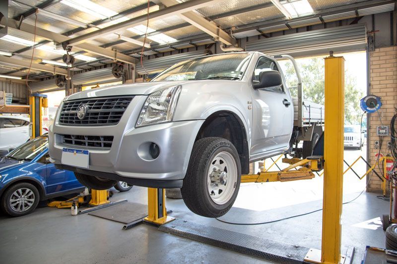 Silver SUV lifted on a car jack in an auto repair shop with a blue car nearby