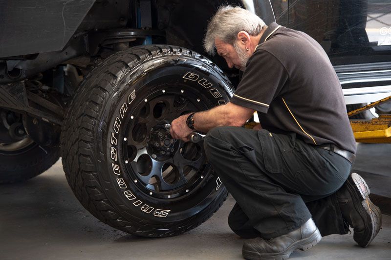 Mechanic crouches by a truck wheel, tightening lug nuts in a garage.