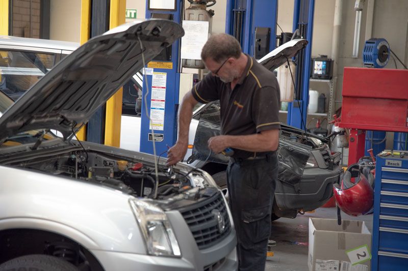 Mechanic working on a silver car with hood open in an auto repair shop