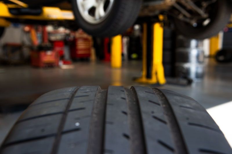 Close-up of a car tire tread in an auto repair shop with a lifted vehicle in the background