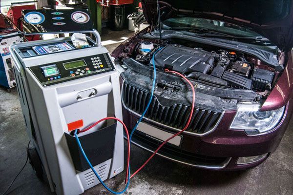 Car battery charging and diagnostic test in a garage, with red cables connected to a maroon car