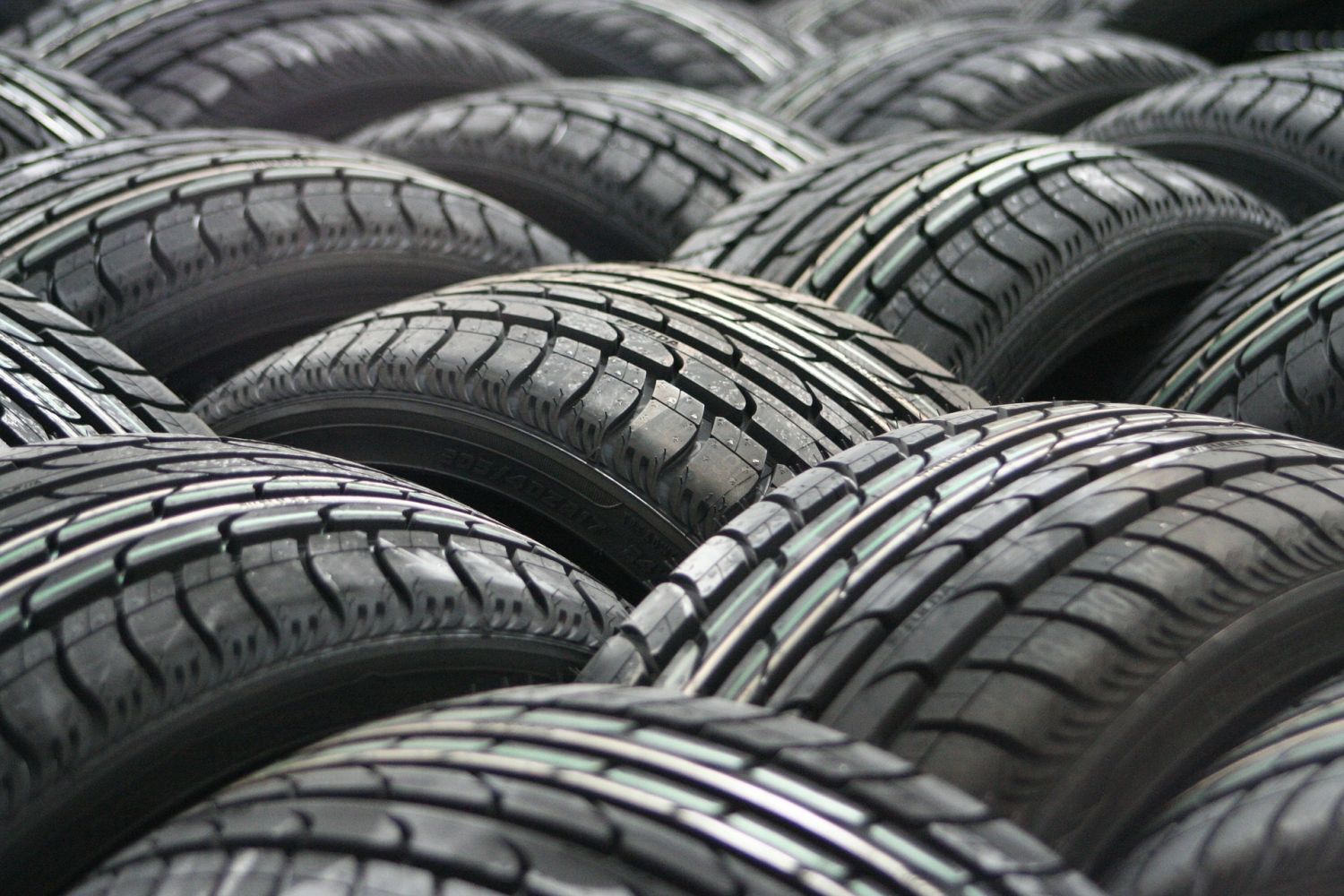 Stacks of black car tires with tread patterns visible, arranged in rows at a tire lot