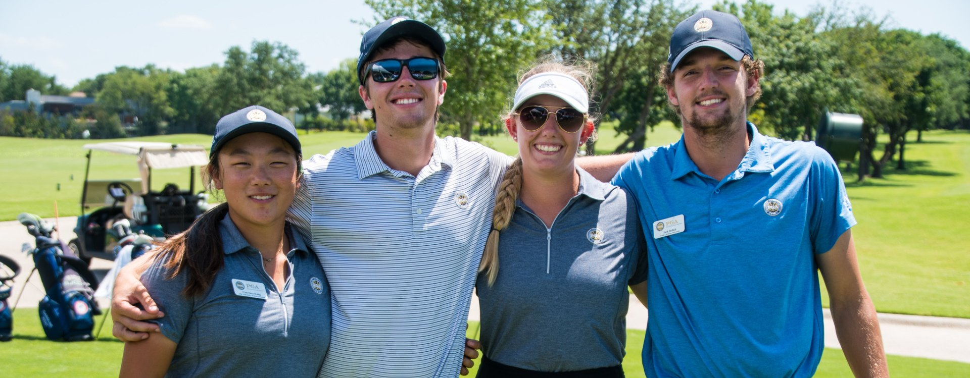 Four smiling golfers standing together on a sunny golf course, arms around each other.