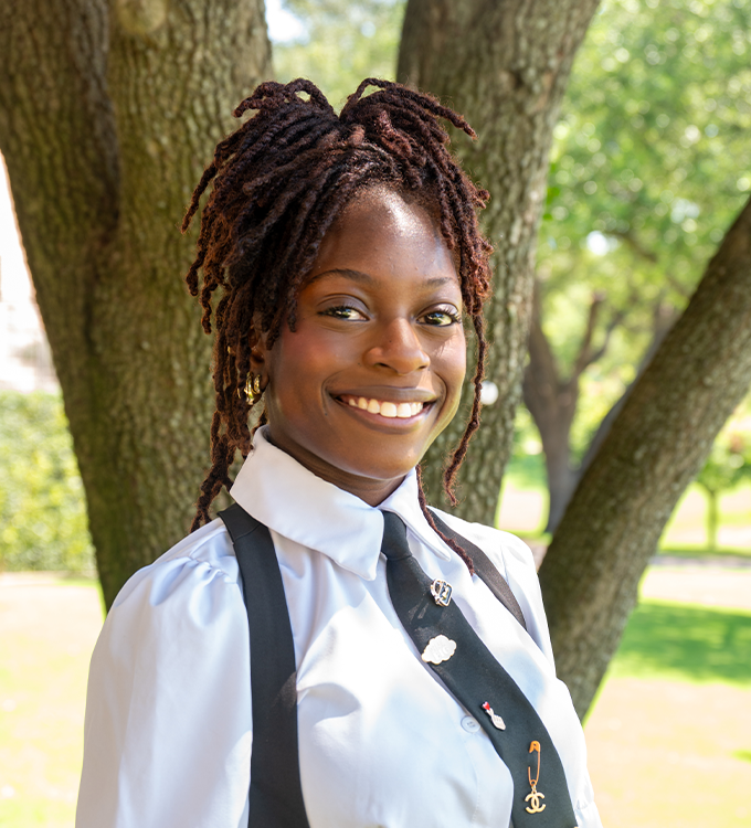 Smiling person in white shirt and black tie standing outdoors by a tree