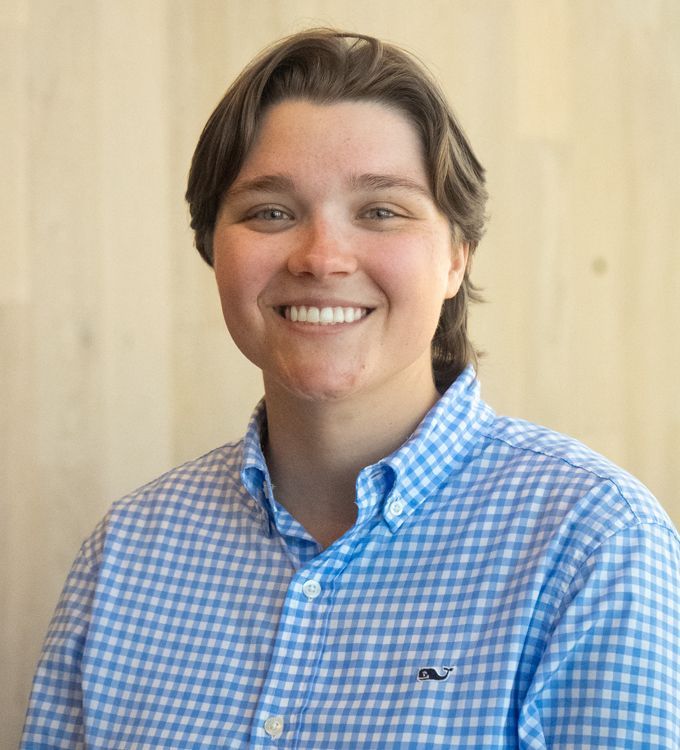 Smiling person in a blue checkered shirt against a light wood background