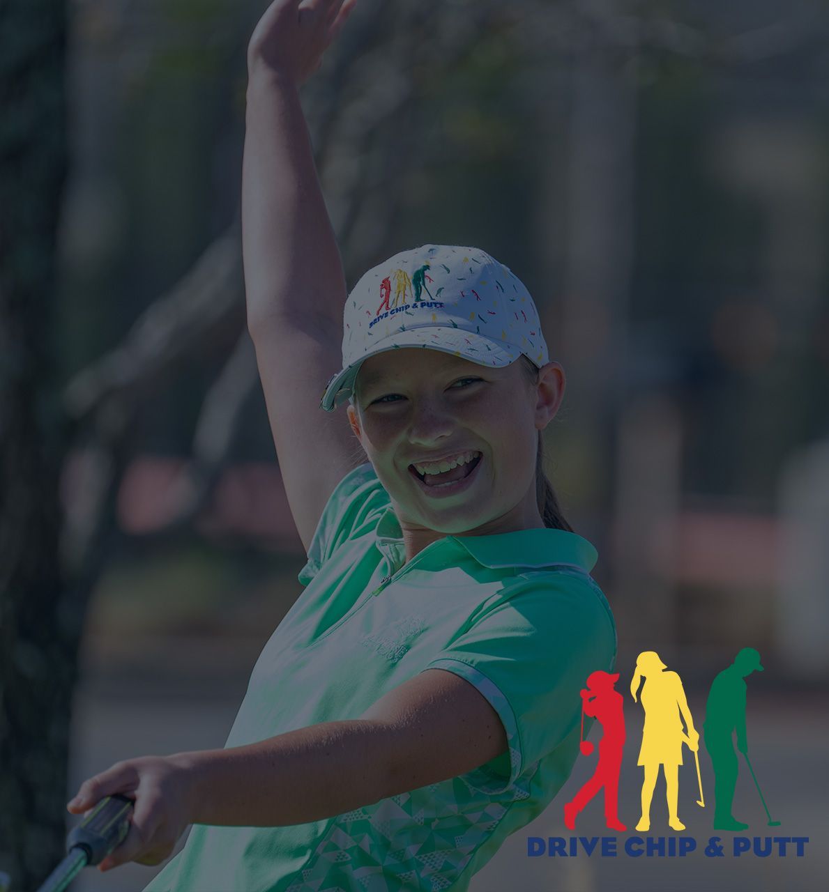 Golfer in green shirt and white cap posing with arms raised, holding a club at Drive Chip & Putt event