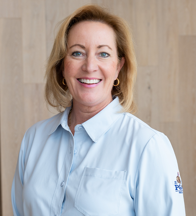 Smiling woman in a light blue shirt standing against a wood-paneled wall