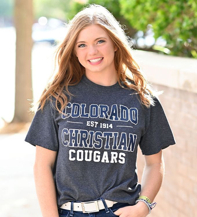 Smiling person in a dark Colorado Christian Cougars T-shirt standing outdoors in sunlight