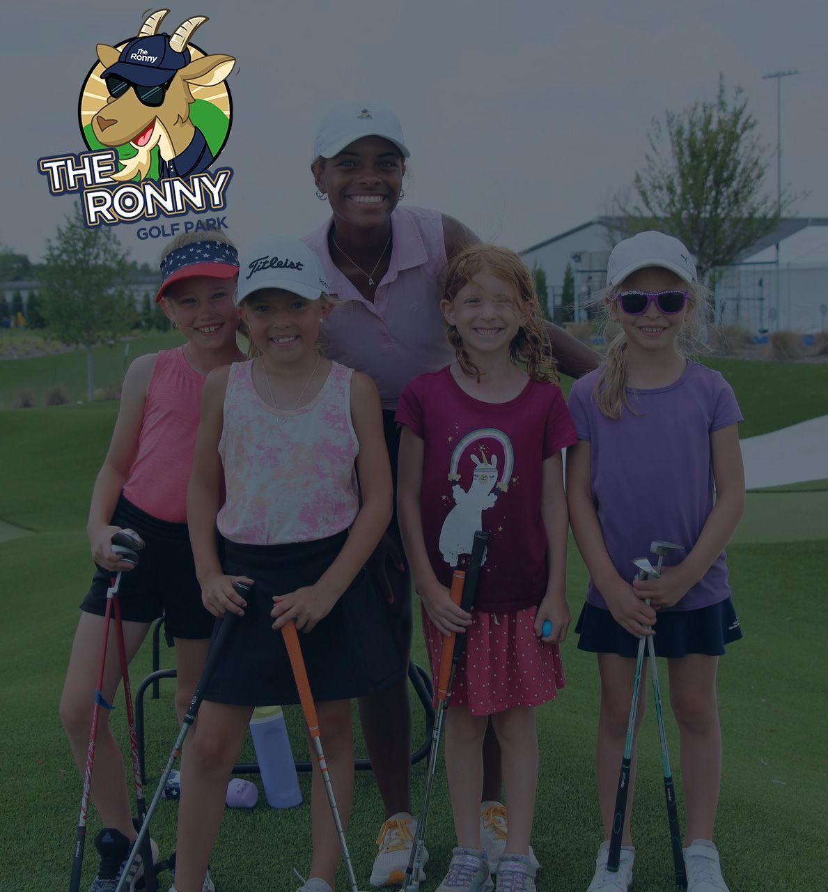 Five children and an adult posing with golf clubs on a green at an outdoor event