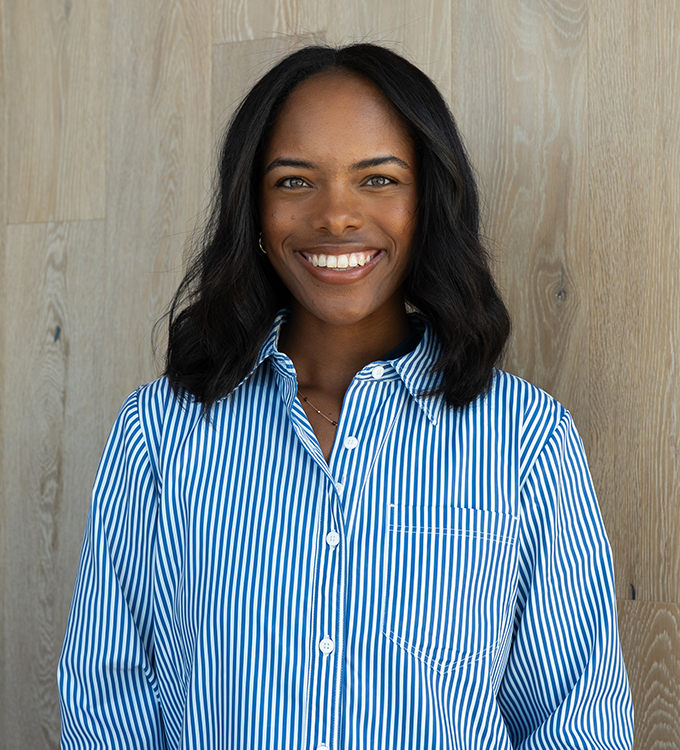 Smiling woman in a blue striped shirt standing against a wooden wall