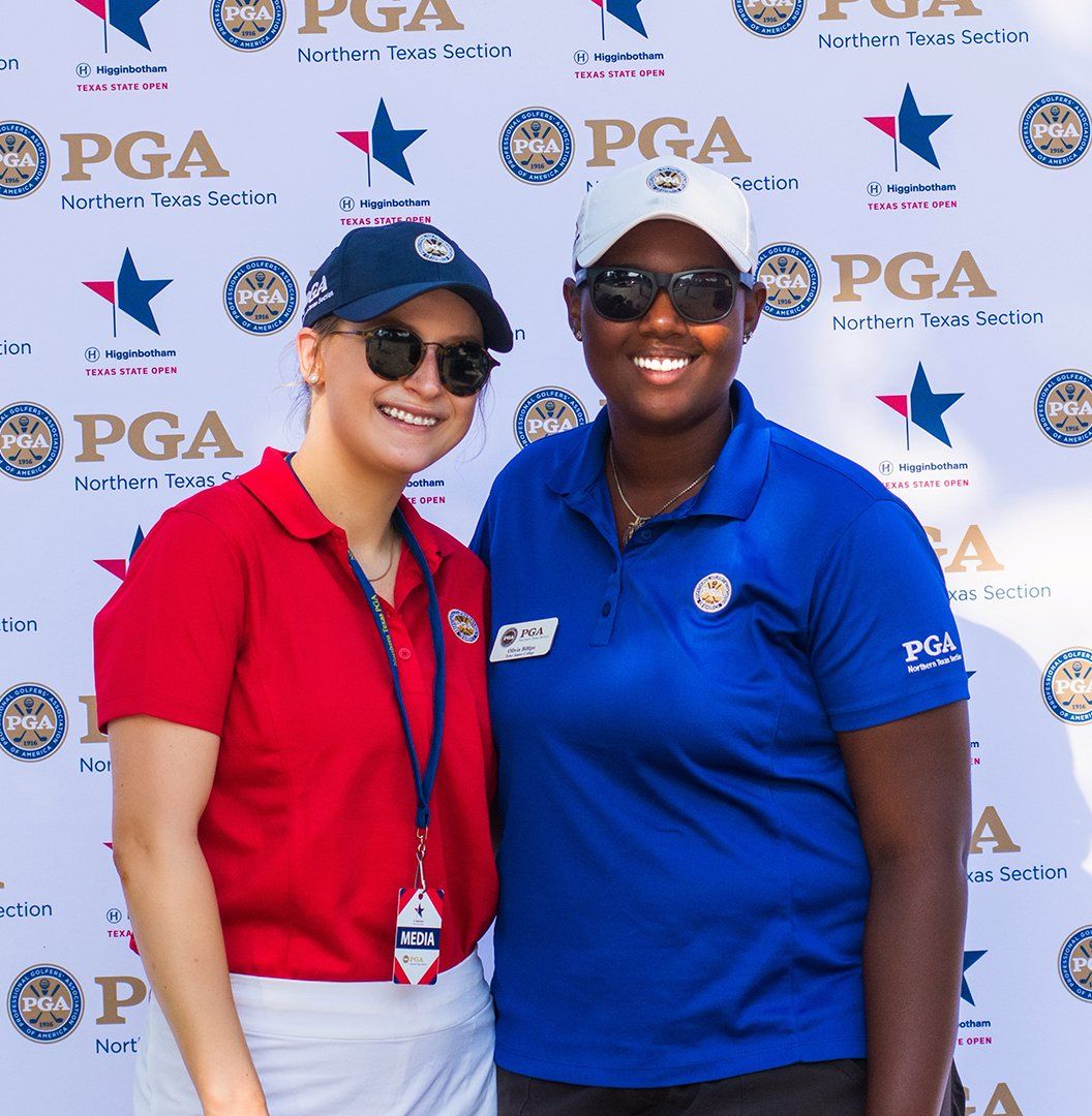 Two PGA staff members posing in front of a PGA backdrop, one in red and one in blue.