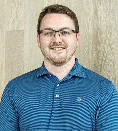 Smiling person in glasses and a blue striped polo shirt against a light wood background