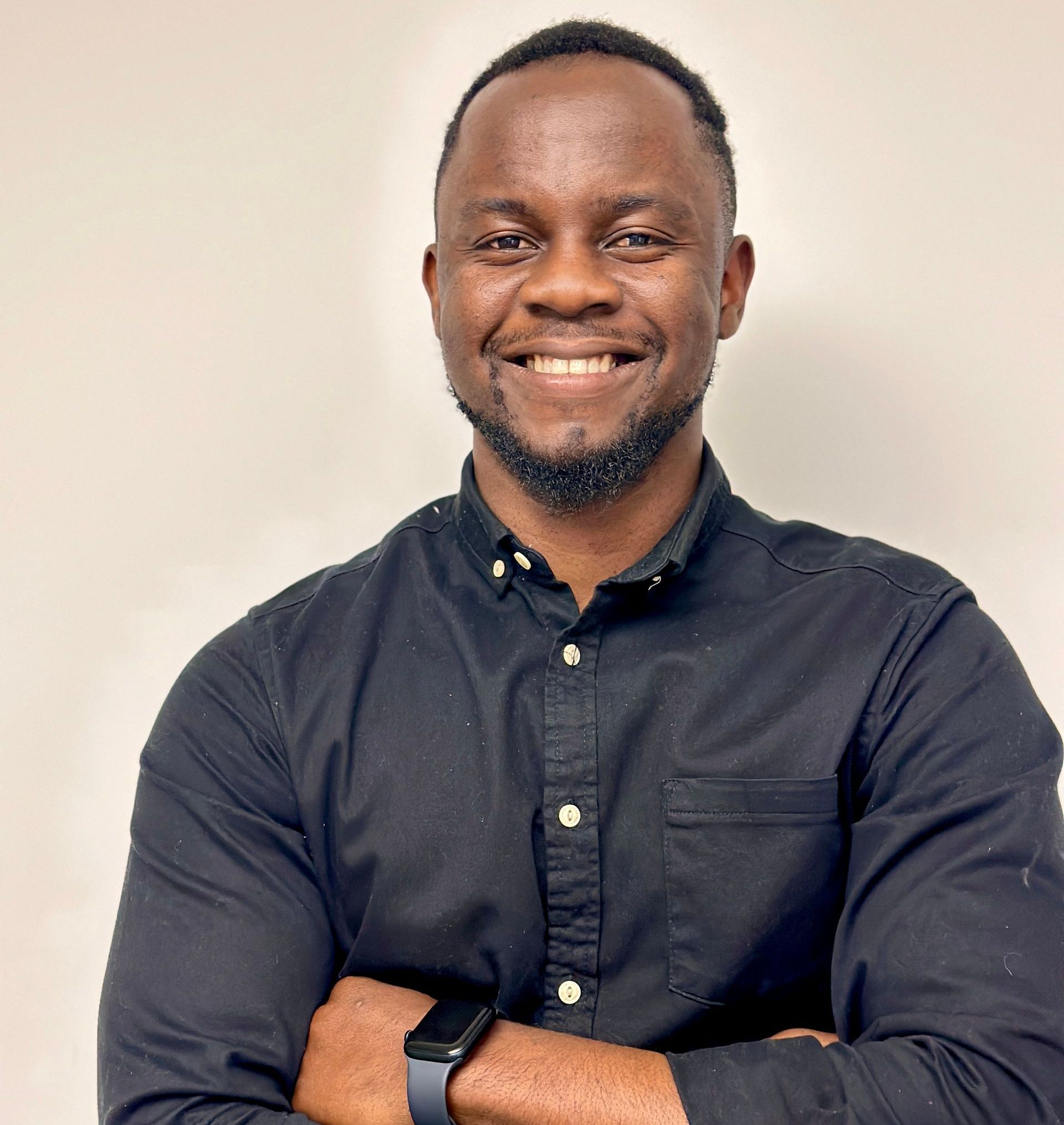 A man in a black shirt is smiling with his arms crossed.