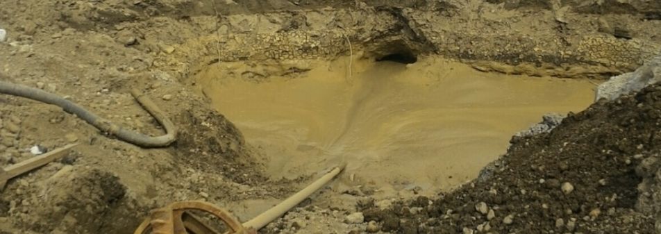 A hole in the ground with a hose and a shovel in it.