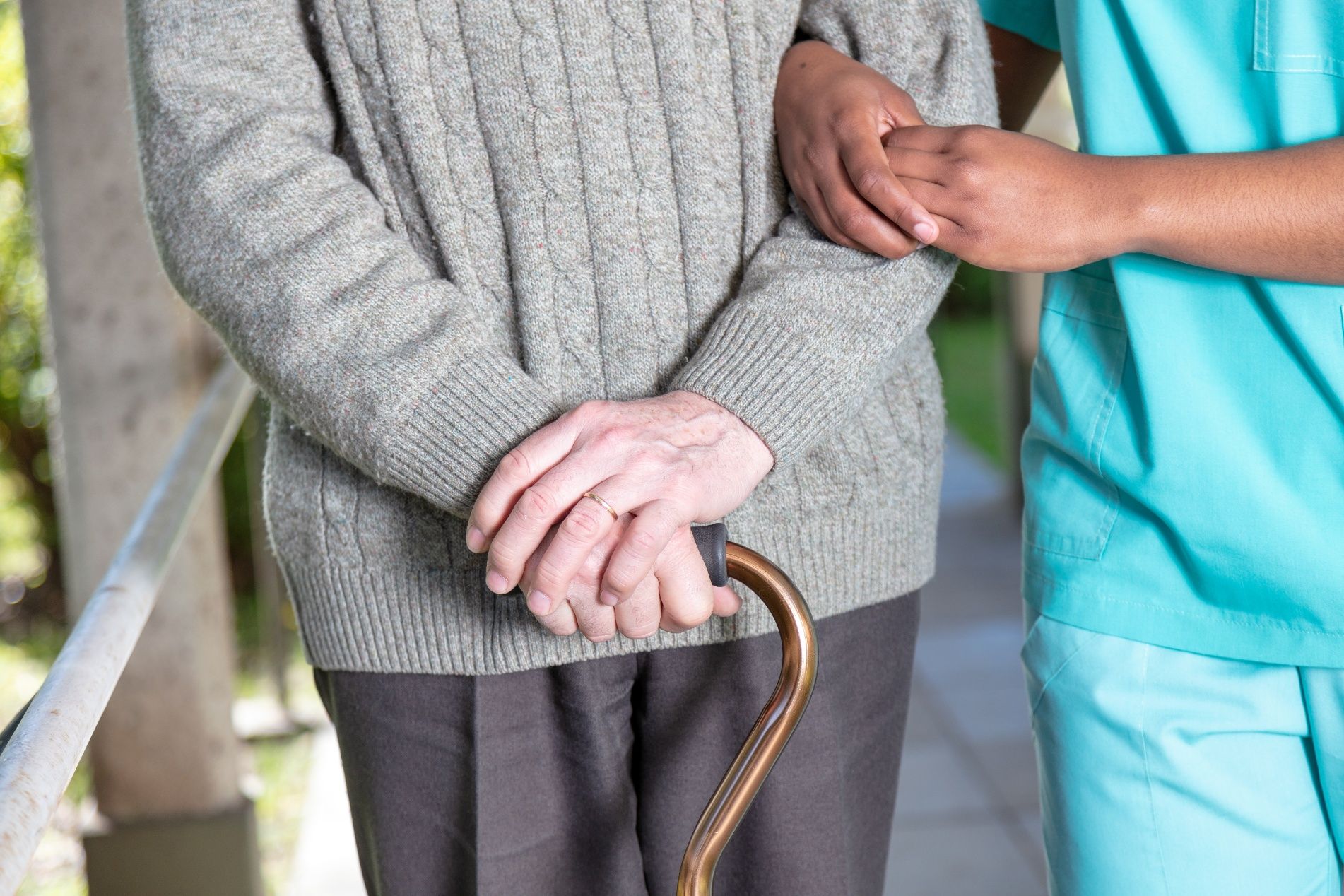 Person using a cane, being assisted by another person, walking.