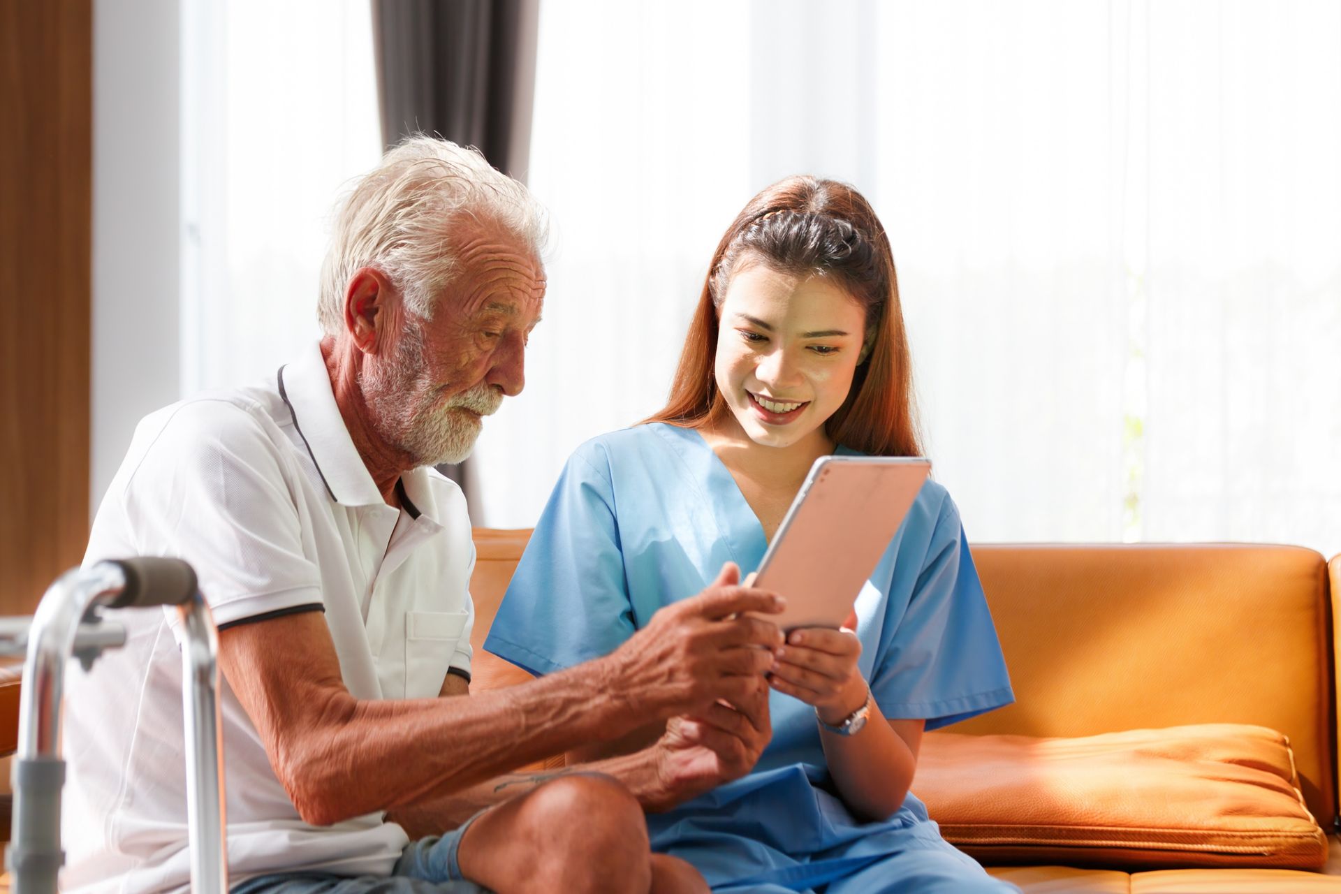 Nurse and older adult looking at tablet on a couch; indoor setting.