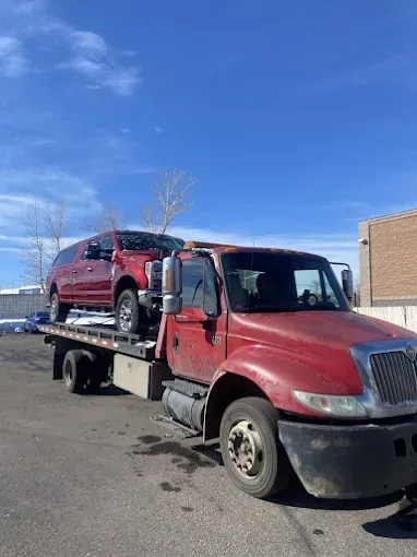Red tow truck carrying a red SUV on a sunny day, parked in a lot.