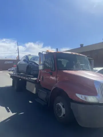 A red tow truck carrying a gray car on a sunny day.