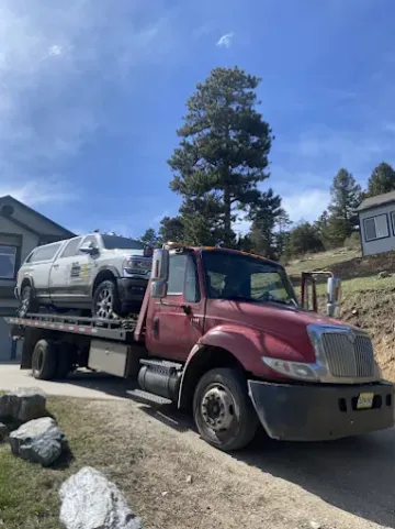 Tow truck carrying a white pickup truck on a sunny day in front of a house.