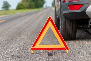 Emergency triangle on road next to a disabled red car, signaling caution.